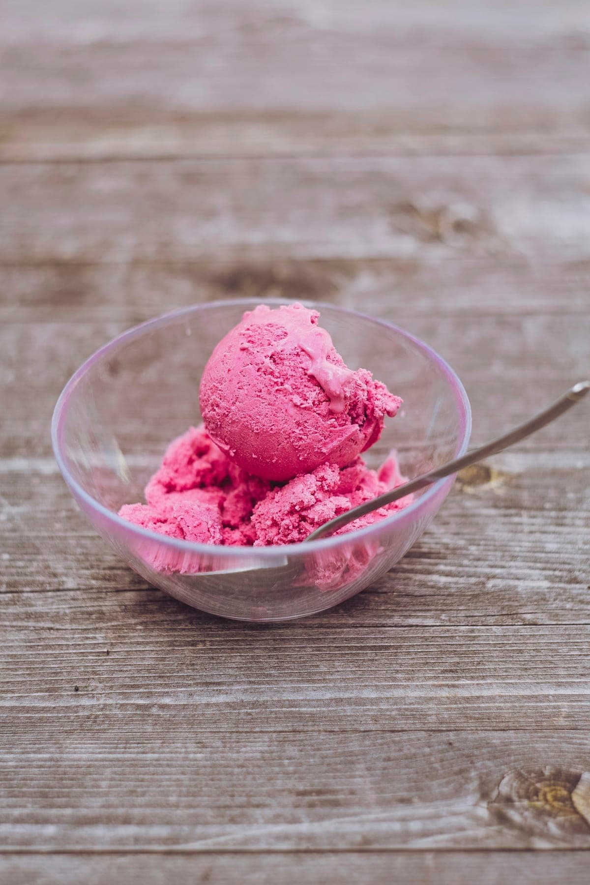 Scoops of berry custard in a glass bowl on a sun-bleached picnic table